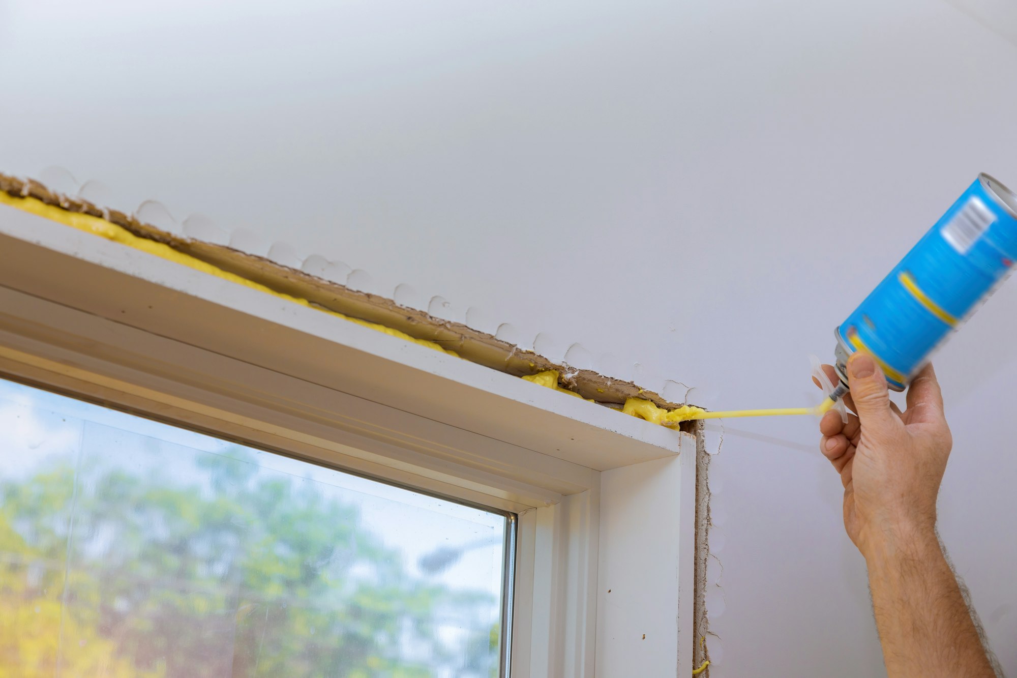 Man in a using a mounting foam the window and the wall with insulation foam to insulate